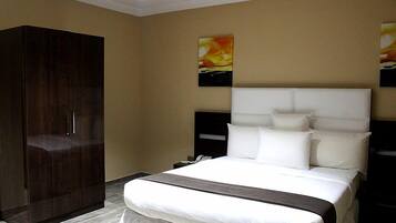 A hotel room with a large bed, a wardrobe, and two wall-mounted nightstands.
