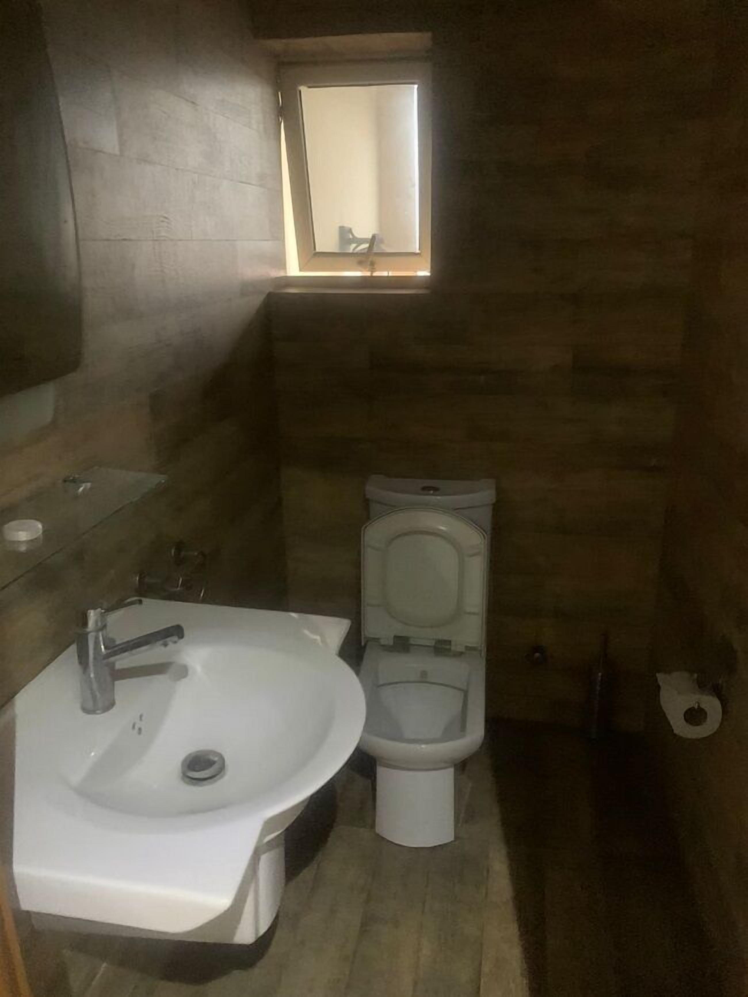 Un baño pequeño con un lavamanos blanco, un inodoro y una ventana sobre el inodoro.