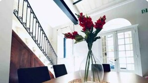 Ein Esstisch mit einer klaren Glasvase, in der rote Blumen stehen, einer gewebten Tischmatte und schwarzen Stühlen.