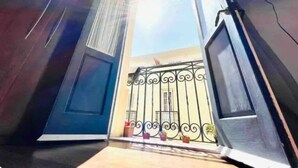 Ein Zimmer mit großem Fenster, einer Tür und einem Balkon mit schmiedeeisernem Gitter.