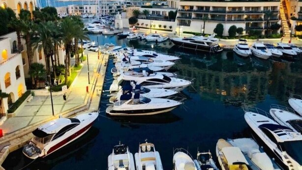 Eine Marina mit mehreren Yachten, umgeben von modernen Gebäuden und Palmen.