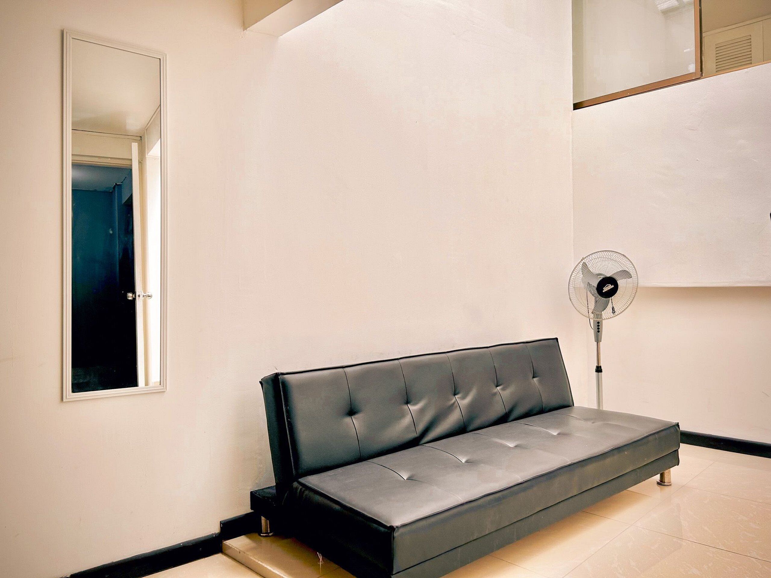 A modern room with a grey sofa, a standing fan, and a mirror on the wall.