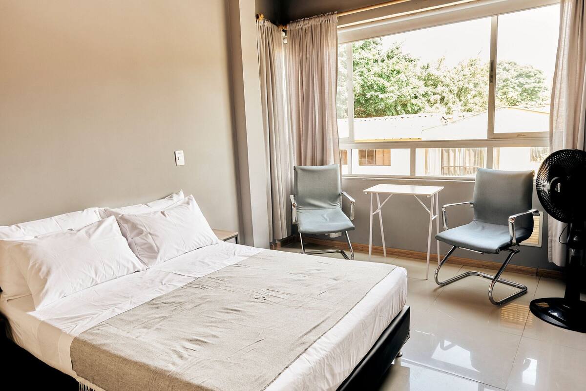 Een hotelkamer met een bed, twee stoelen, een kleine tafel en een raam met gordijnen.