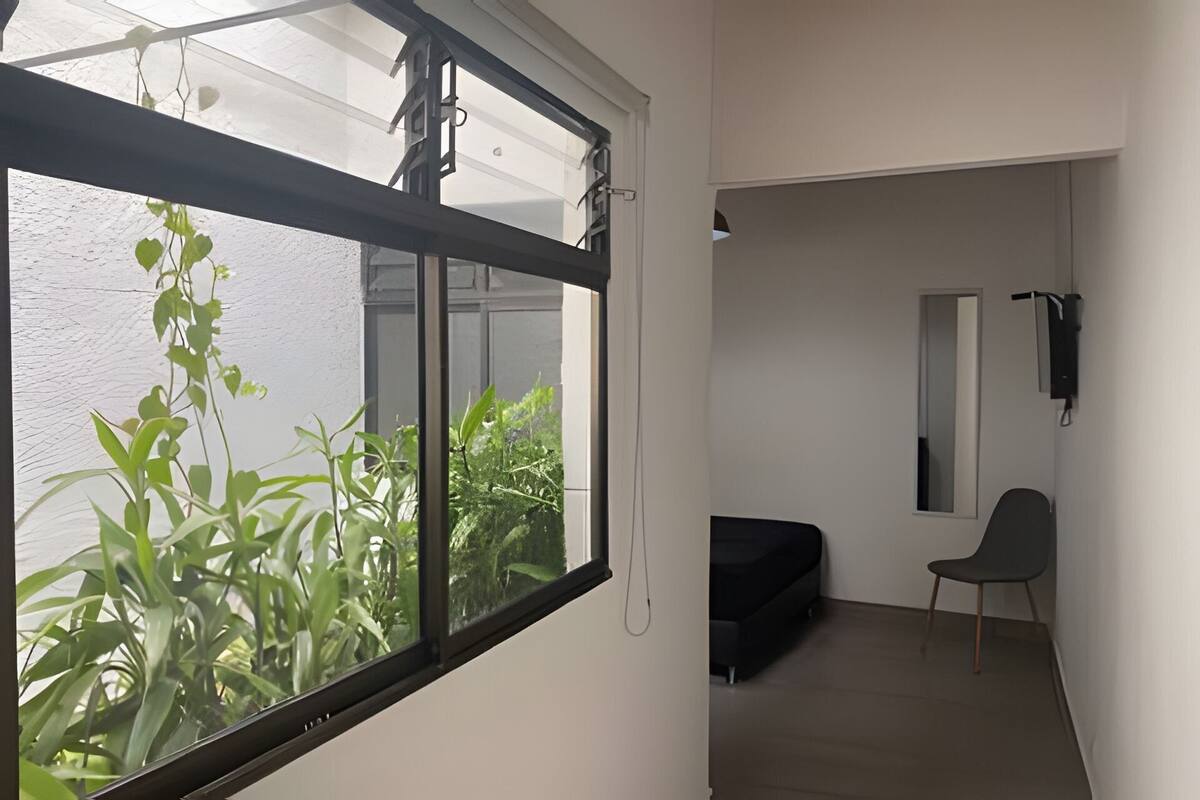 Een kamer met een groot raam, een zwarte bank, een stoel en een spiegel aan de muur.
