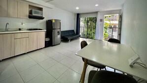 Een moderne keuken met een magnetron, koelkast en spoelbak. Er is een eethoek met een tafel en stoelen. De kamer heeft een balkon met uitzicht op groen.