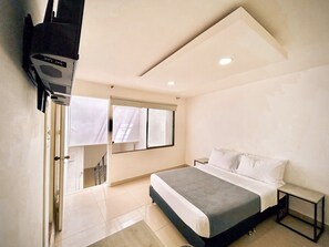 A modern bedroom with a bed, a small bedside table, a mirror, and a shower area. - Vivvo Espacios La 80 (Medellín)