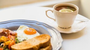 Un plato de desayuno con huevos, tocino, tostadas y una taza de té sobre una mesa blanca.