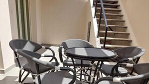 Un ensemble de chaises et de tables d’extérieur disposées autour d’un sol en béton, avec un escalier et une porte en arrière-plan.