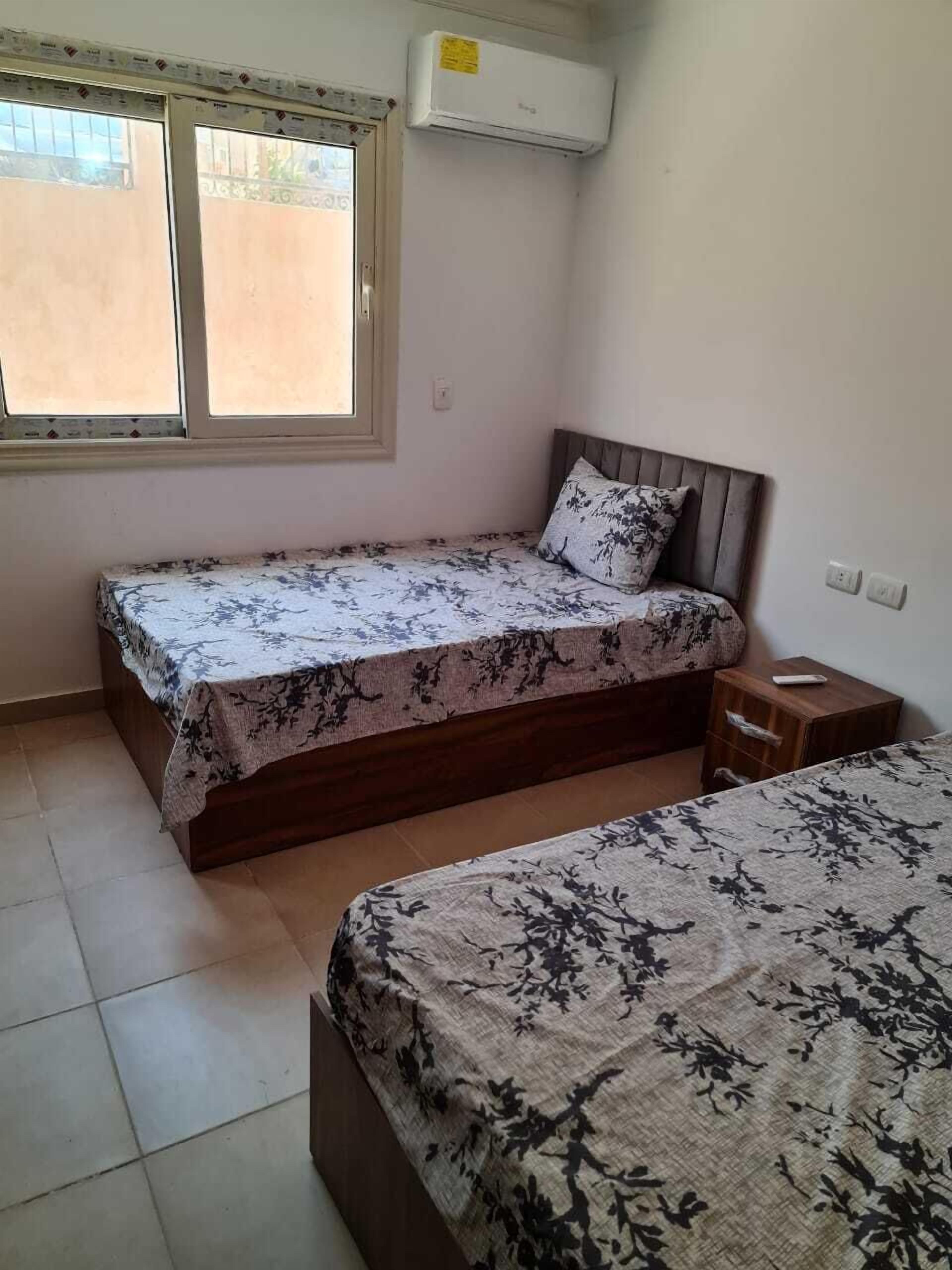 A bedroom with two single beds, a window, and an air conditioner.