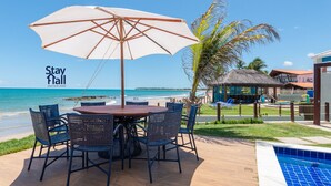 Una terrazza fronte spiaggia con tavolo e sedie, una piscina e una capanna con tetto di paglia.