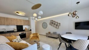 Ein modernes Wohnzimmer mit einer Couch, einem Couchtisch und einem Esstisch. Es gibt eine Küchenzeile mit Holzschränken und einem flachbildfernseher, der an der Wand befestigt ist.