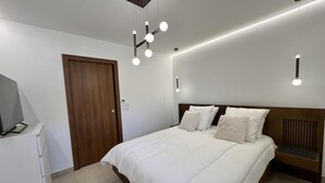 Ein modernes Schlafzimmer mit einem großen Bett, einem Holz-Kopfteil, einem Fernseher auf einem Schrank und einer Deckenleuchte.