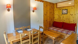 A cozy room with a wooden dining table set for two, a bench with red cushions, and a wooden wall with a picture. - 40m from ski slopes, 3rd floor, fitness, swimming pool, sauna, balcony, tv, ski locker, 35m² (Les Orres)