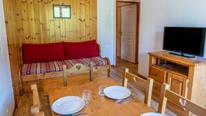 A wooden room with a sofa, a TV, and a dining table set with plates and glasses. - 40m from ski slopes, 3rd floor, fitness, swimming pool, sauna, balcony, tv, ski locker, 35m² (Les Orres)