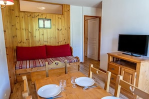 A wooden room with a sofa, a TV, and a dining table set with plates and glasses.