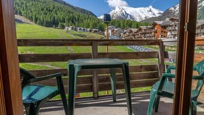 A balcony with green plastic chairs and a table, overlooking a mountainous landscape with a ski resort in the background. - 40m from ski slopes, 3rd floor, fitness, swimming pool, sauna, balcony, tv, ski locker, 35m² (Les Orres)
