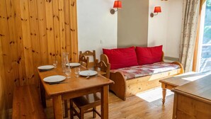 Ein gemütliches Zimmer mit einem Holzespeisetisch, gedeckt für zwei Personen, einer Holzbank und einem Sofa mit roten Kissen.