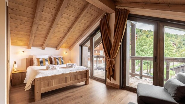 A wooden bedroom with a large bed, a nightstand, a window with curtains, and a balcony with a view of greenery. - 3rd floor, view mountain, balcony, parking, tv, ski locker, 123m², Montalbert (La Plagne)