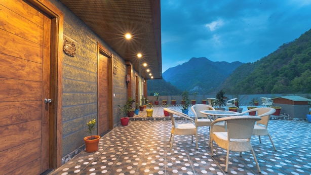 A covered outdoor seating area with a patterned floor, wooden walls, and a view of a mountain. - Riviera Resort  Rishikesh (Yamkeshwar)