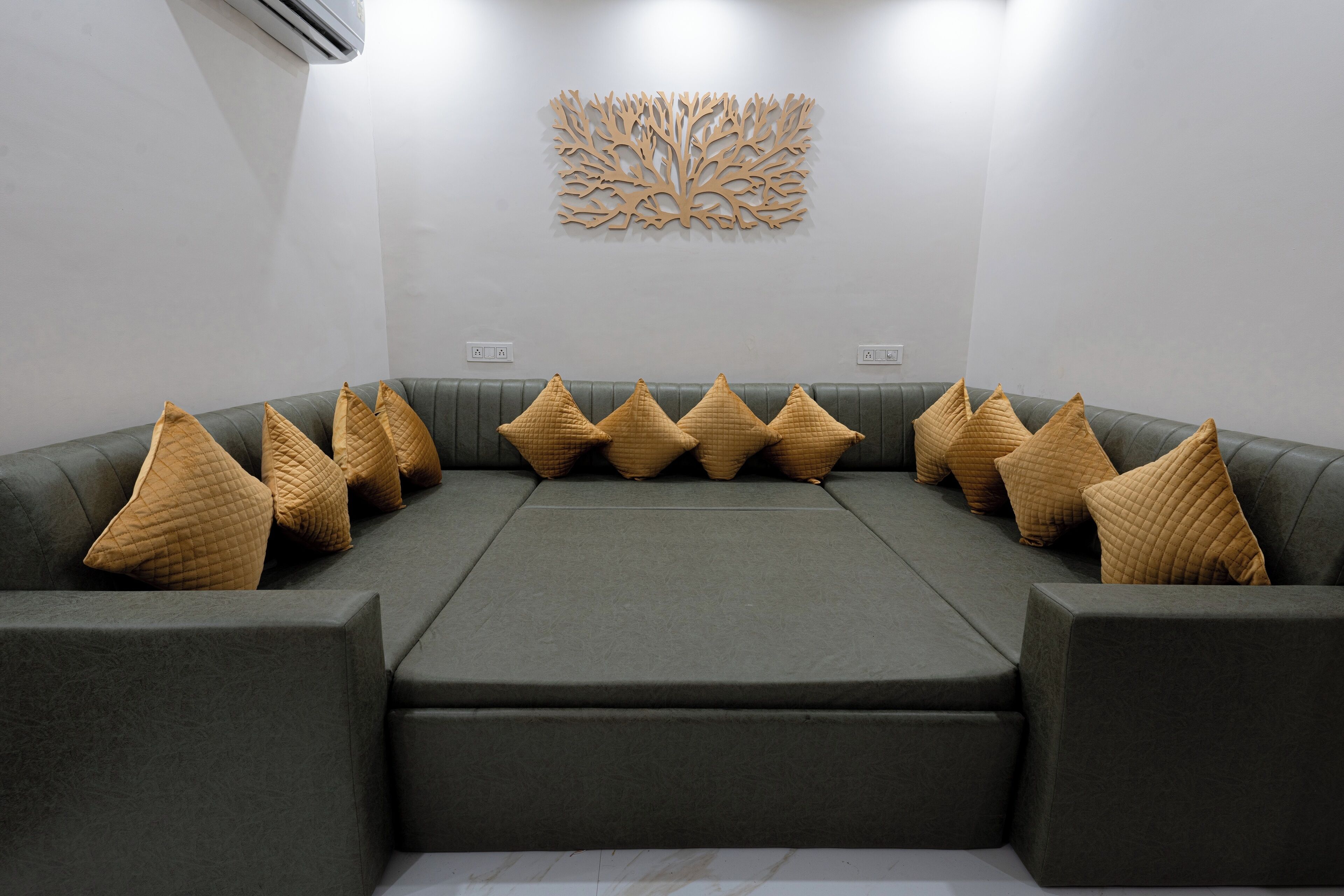 Une pièce moderne et bien éclairée, avec un canapé d’angle gris et de nombreux coussins, un élément décoratif mural et un design épuré et minimaliste.