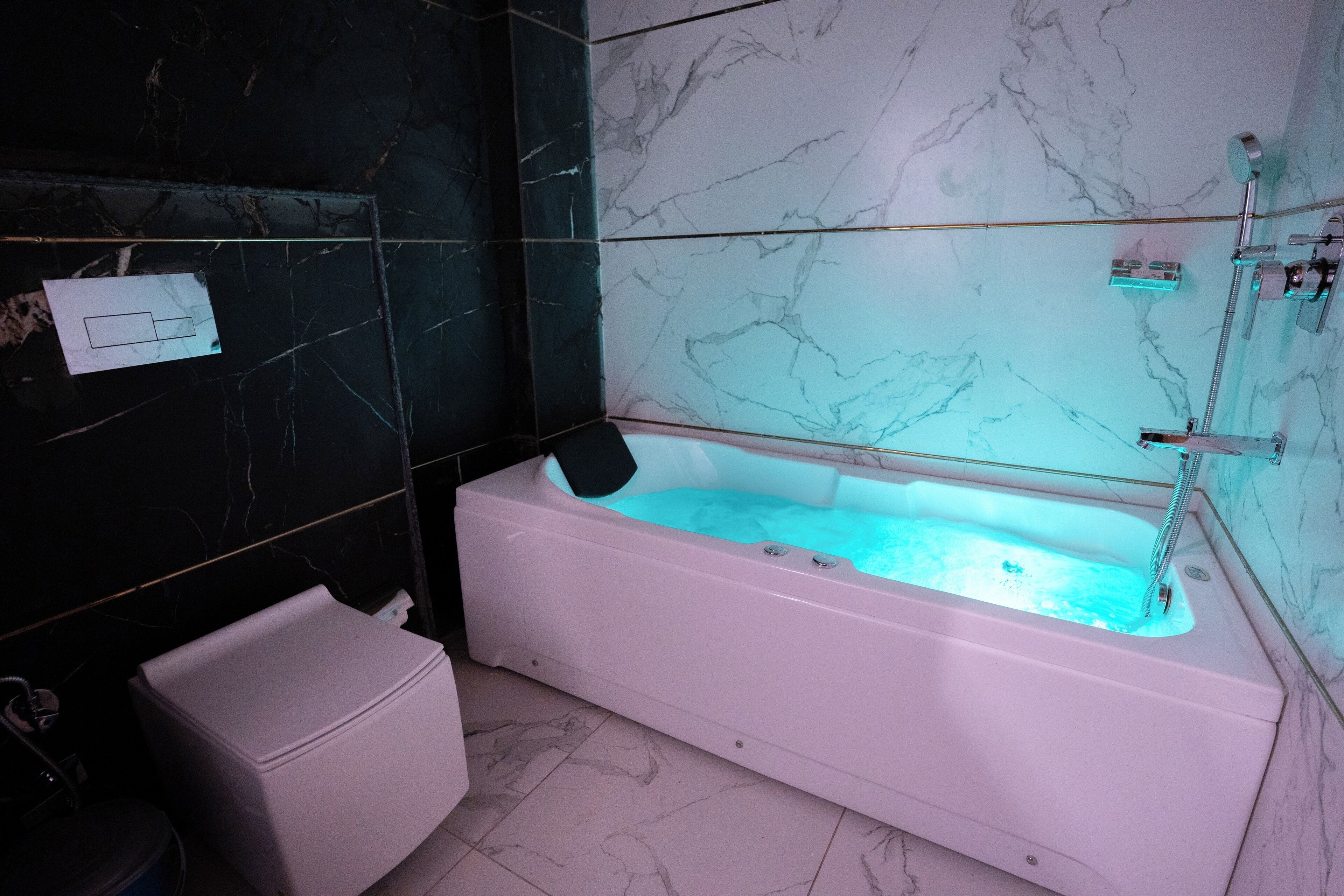 A modern bathroom with a white bathtub, black and white marble walls, and a white toilet.
