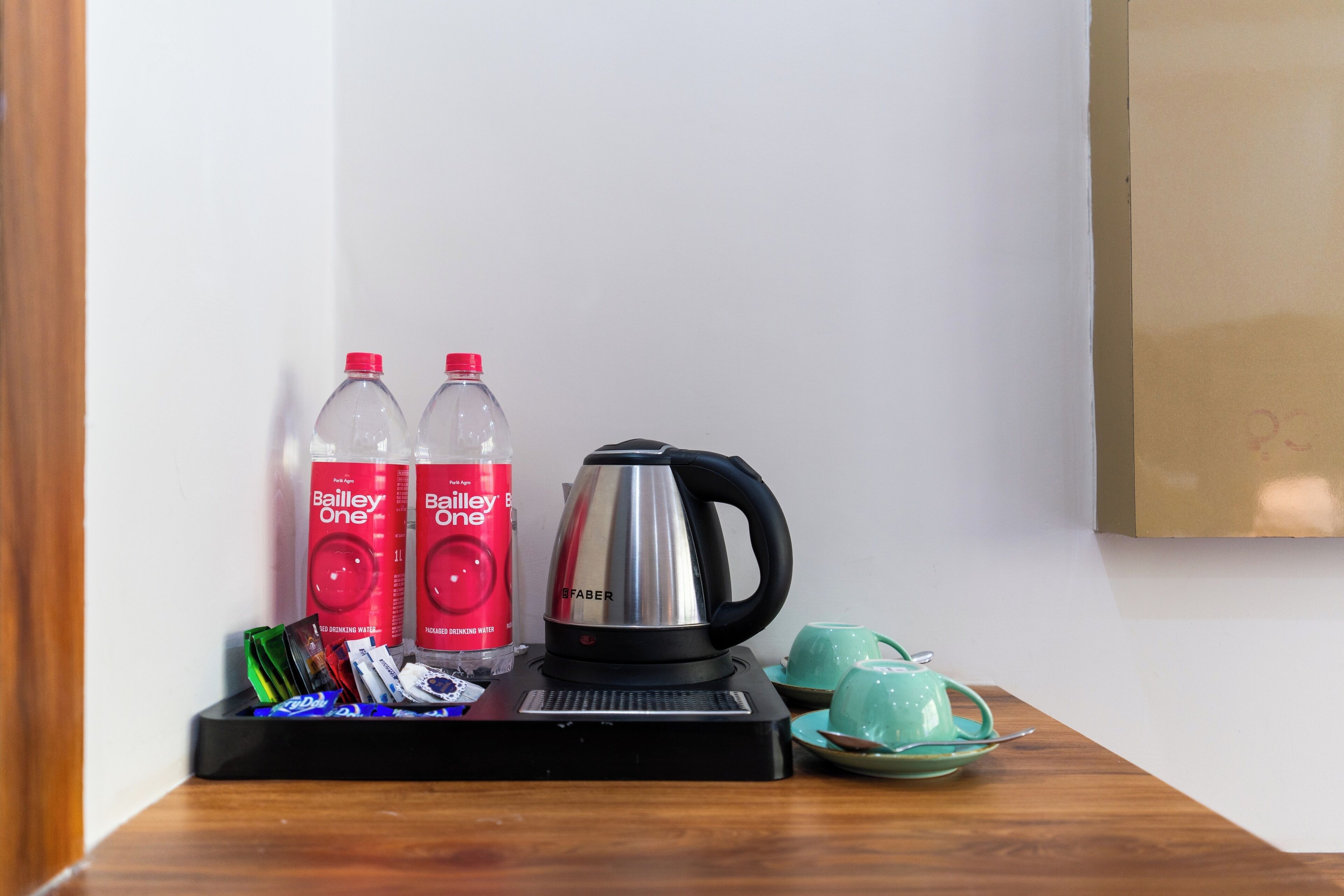A tray with Bailey's One beer bottles, a silver electric kettle, and a green teapot on a wooden table.