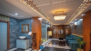 A modern lobby with a marble floor, a wooden reception desk, a blue sofa, and a chandelier. - Riviera Resort  Rishikesh (Yamkeshwar)