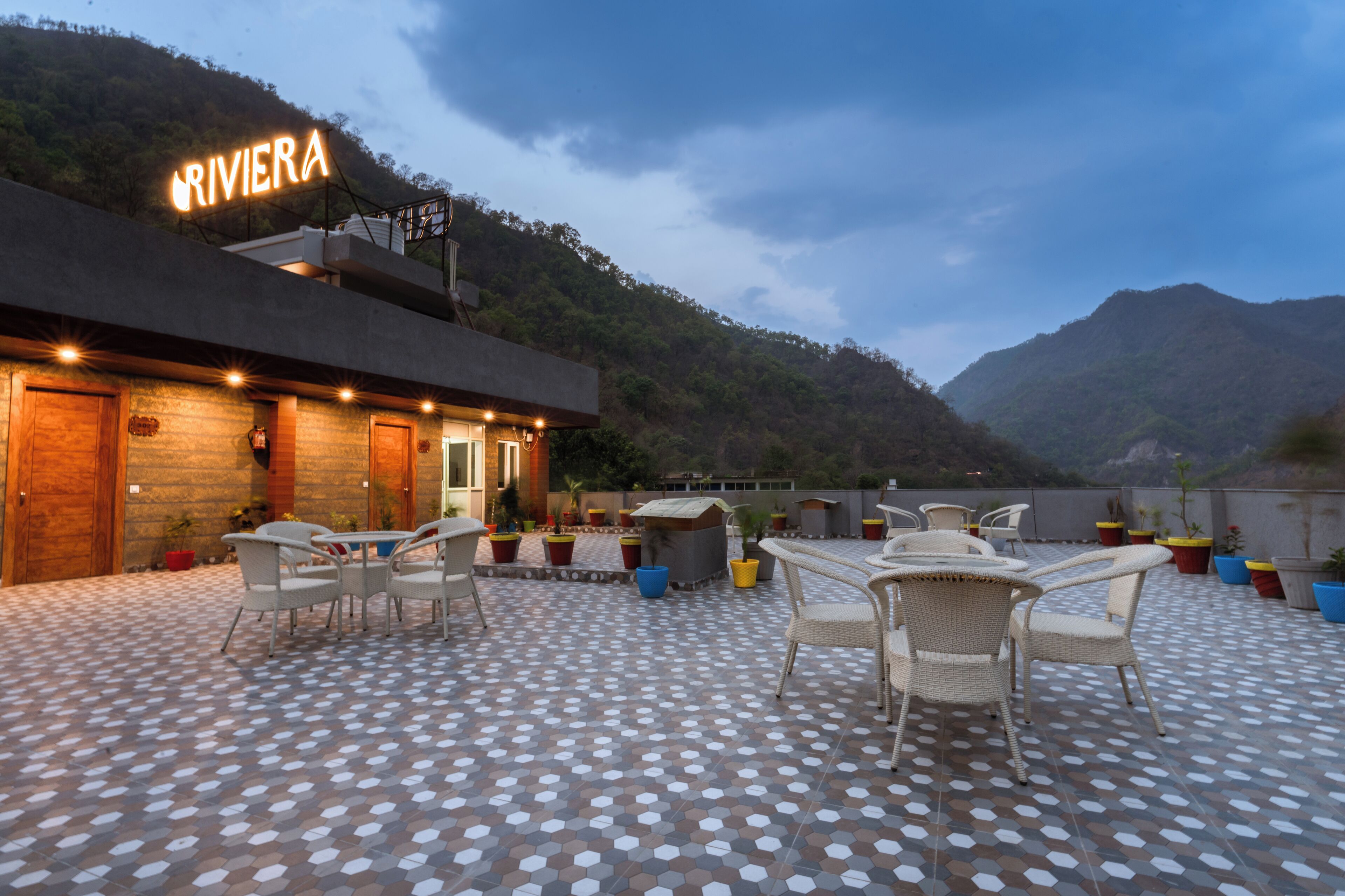 A rooftop patio with outdoor seating, a sign reading "RIVIERA," and a mountainous backdrop.