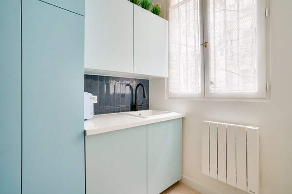 Una cocina moderna con encimera blanca, grifo negro y ventanal con vidrio esmerilado.