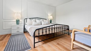 A bedroom with a bed, bedside tables, a nightstand, a rug, and a wooden bench. - Gay Street Retreat - Walk to Campus & Downtown (Auburn)