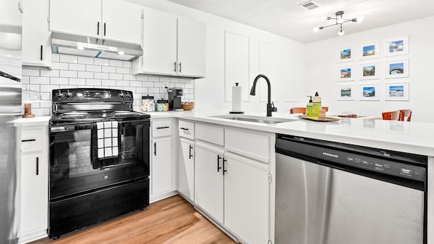 A modern kitchen with white cabinets, a black stove, and a stainless steel dishwasher. - Gay Street Retreat - Walk to Campus & Downtown (Auburn)
