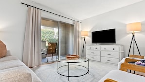 A modern hotel room with a glass table, a flat-screen TV, a white dresser, and a sofa. - Gay Street Retreat - Walk to Campus & Downtown (Auburn)