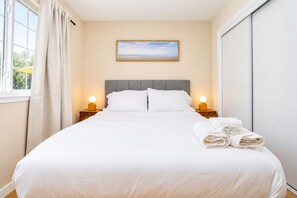 A neatly made bed with white linens, two bedside lamps, a painting on the wall, and a window with curtains. - Stylish Mid-Century Family 4BR Hideaway - San Jose & Milpitas (San Jose)