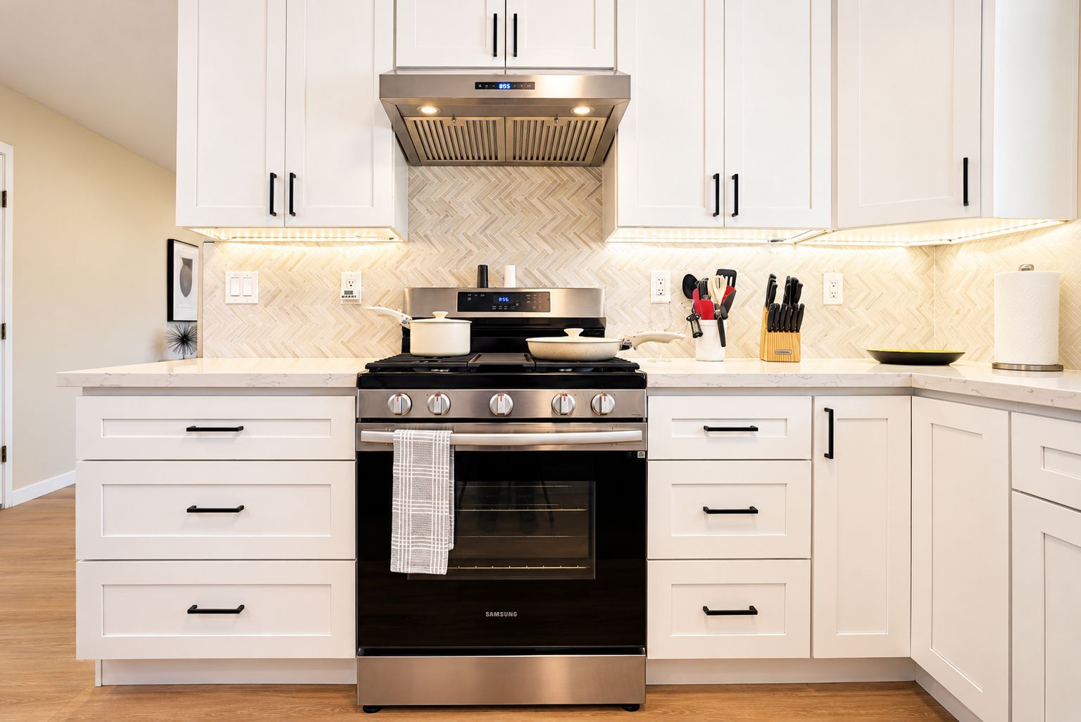 A modern kitchen with white cabinetry, a stainless steel range hood, and a Samsung oven.