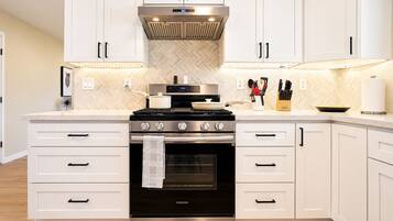 A modern kitchen with white cabinetry, a stainless steel range hood, and a Samsung oven.