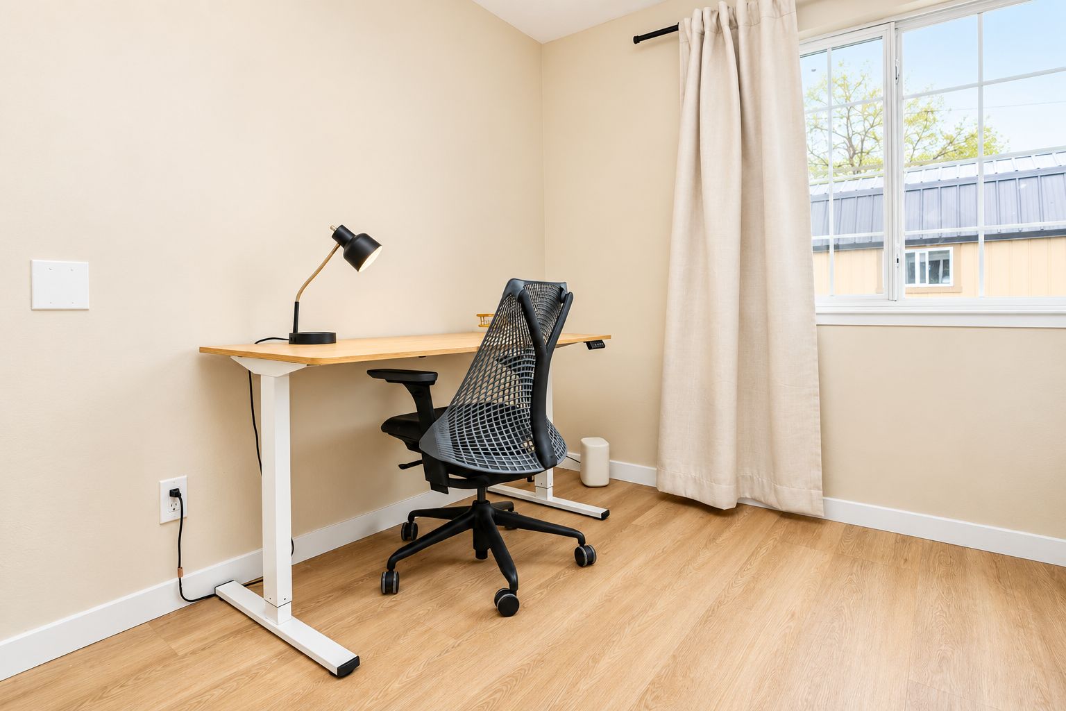 Ett rum med ett skrivbord, en stol, en lampa och ett fönster med gardiner.