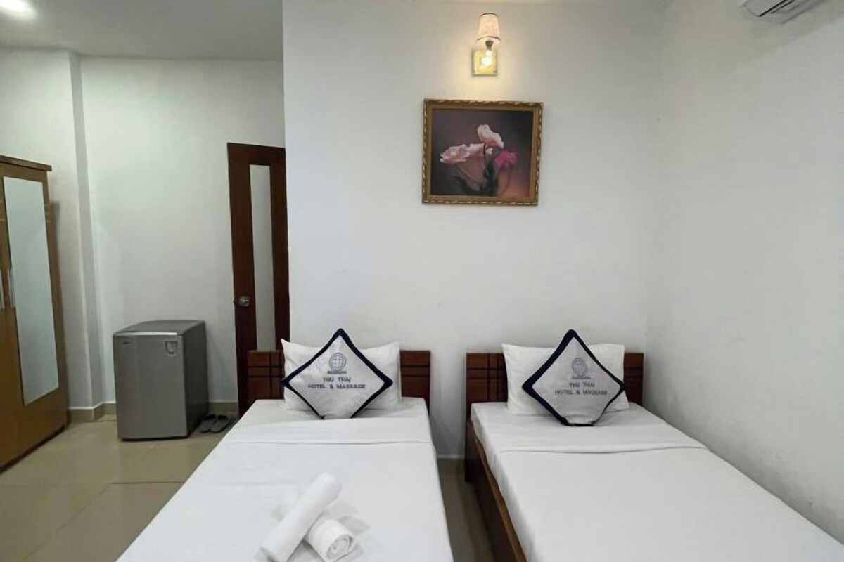 Habitación de hotel con dos camas individuales, un escritorio, una silla, una lámpara de escritorio pequeña, un cuadro en la pared y una puerta.