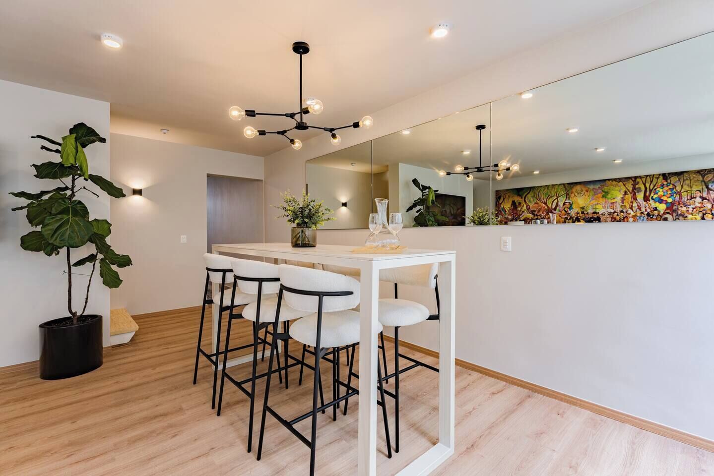 A modern dining area with a white table and black chairs, a potted plant, and a ceiling light fixture.