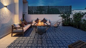 A cozy outdoor seating area with a fire pit, patterned floor tiles, and a wall-mounted light fixture.
