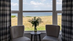 A room with a large window, two chairs, and a small table with a vase of flowers.