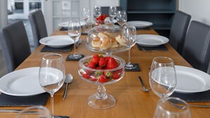 A dining table set with white plates, clear wine glasses, and a bowl of strawberries.