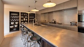 A modern kitchen with a long countertop, stainless steel appliances, and bar stools.