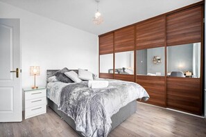 A bedroom with a bed, bedside tables, a mirror, and a wardrobe. - Birmingham Blissful Retreat - 3 Bed House (Birmingham)