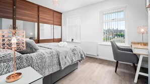 A modern bedroom with a large bed, a desk, and a view of the outside. - Birmingham Blissful Retreat - 3 Bed House (Birmingham)