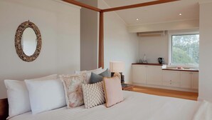 Une chambre avec un grand lit, une table de chevet avec une lampe, un coin cuisine avec des placards et une fenêtre.
