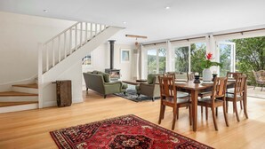 Un vaste salon agrémenté d’un escalier en bois, un coin repas avec des chaises en bois et une grande fenêtre donnant sur un paysage verdoyant.