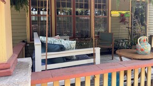 A porch with a white swing chair, a small table, and a decorative vase. - Historical home w gardens in Unique North Lawrence. ACROSS FROM TRAIN DEPOT (Lawrence)