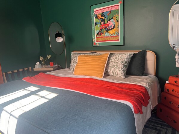A bedroom with a bed, a bedside table, a lamp, a poster, and a suitcase.