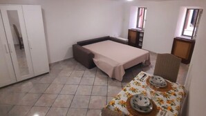 Ein kleines Zimmer mit einem Bett, einem kleinen Tisch mit einer blumigen Tischdecke und einem Kleiderschrank.