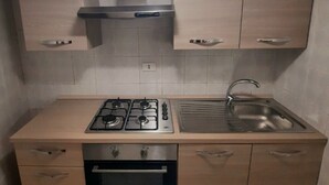 Eine kleine Küche mit Gasherd, Backofen und Spüle. Holzschränke und eine Edelstahl-Dunstabzugshaube sind vorhanden.